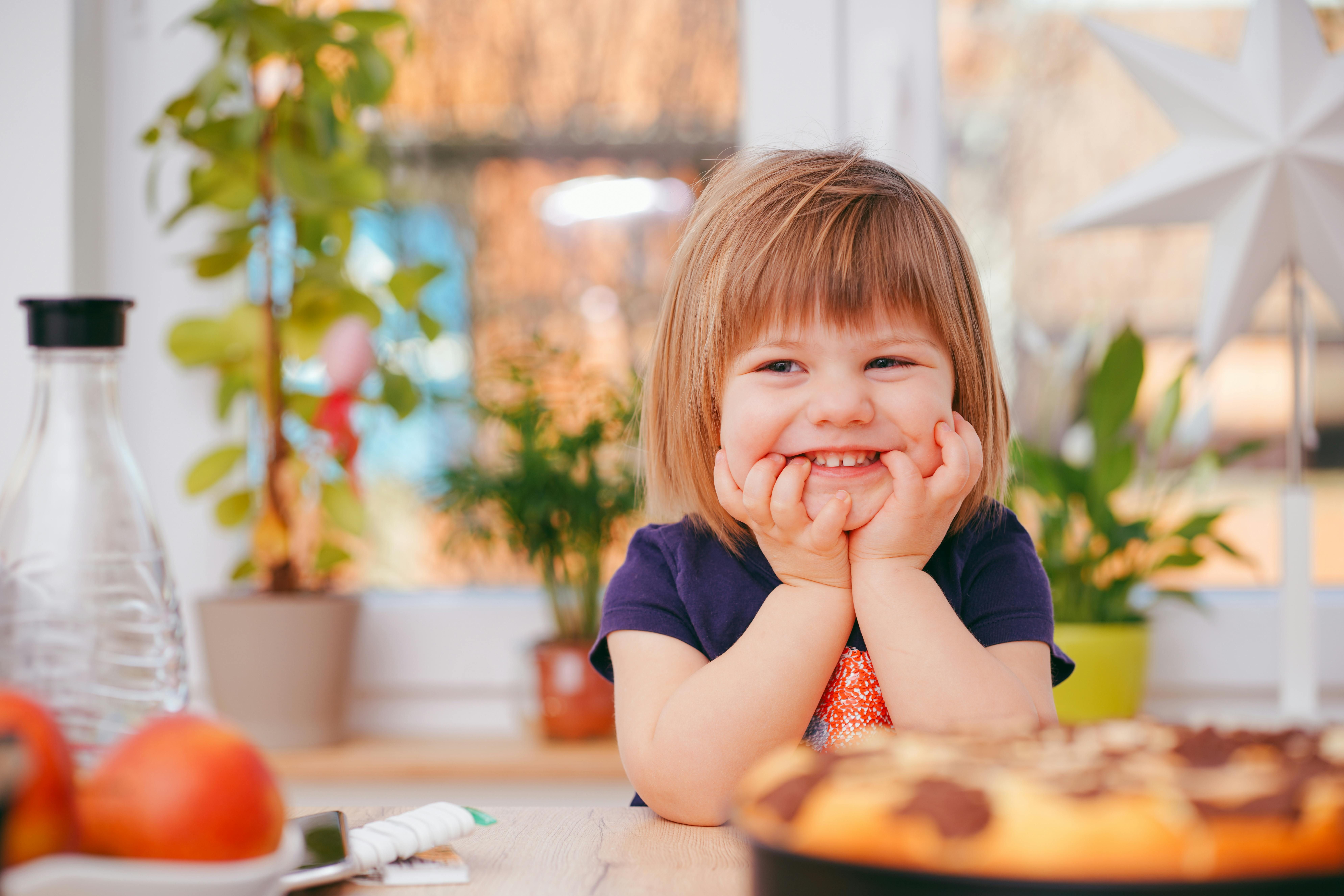 A smiling child with his hands on his chin, looking slightly away from the camera.