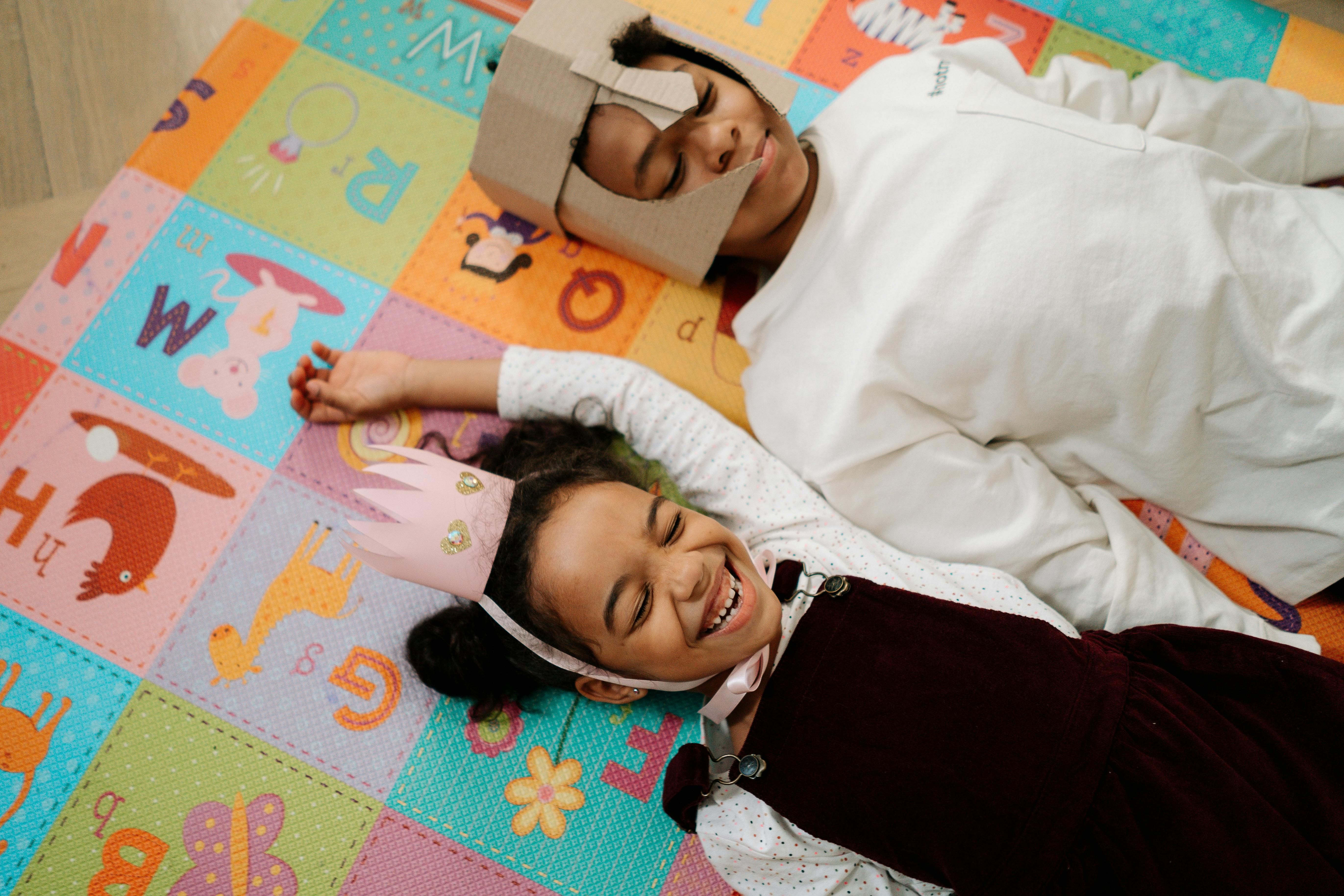 Two children in DIY dress-up laying on the floor laughing.